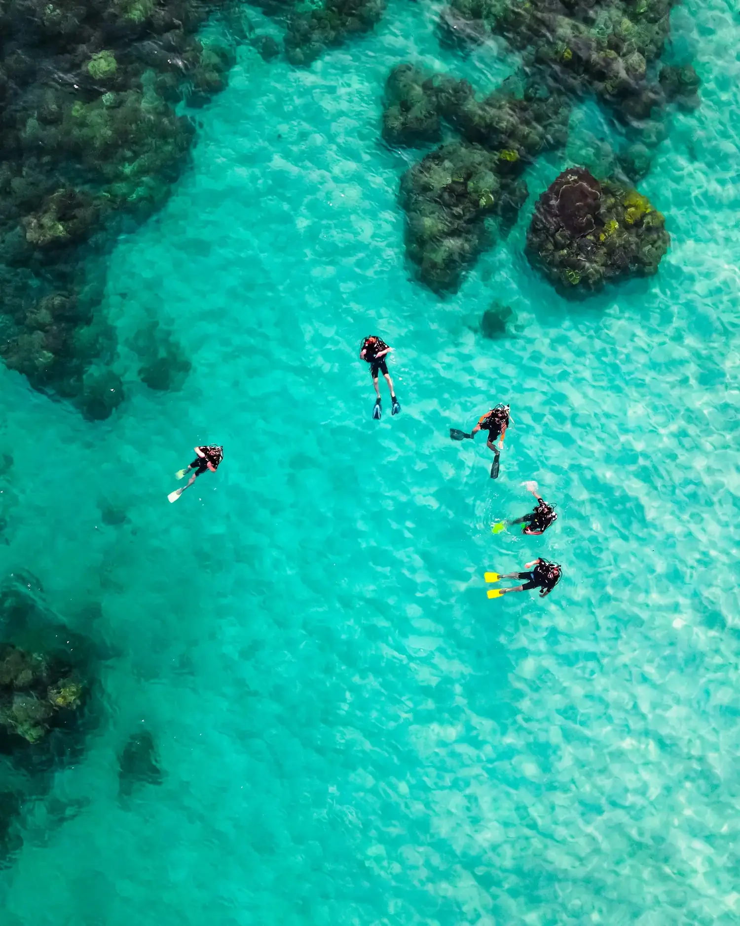 Seen from above: snorkellers spread across bright turquoise shallows beside a reef.