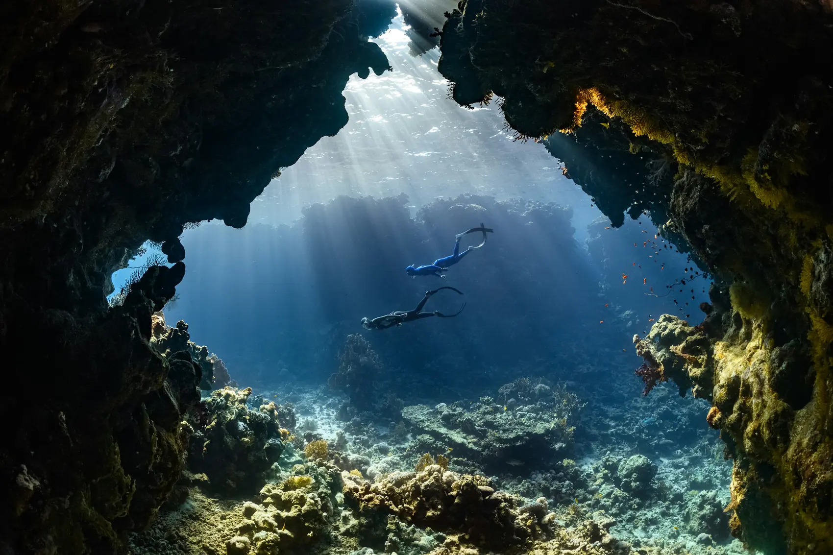 Divers in a cavern with shafts of sunlight falling through the opening above.